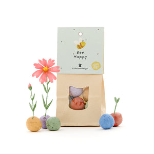 Papiertüte mit der Aufschrift "Bee Happy" und bunten Samenbomben, aus denen Blumen wachsen.