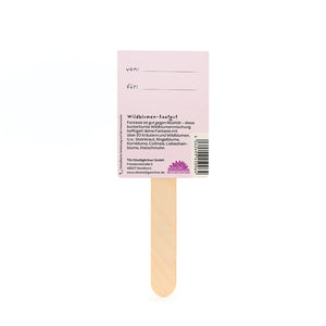 Holzstäbchen mit einem rosa Etikett, auf dem "von" und "für" steht sowie Informationen über Wildblumen-Saatgut auf Deutsch.