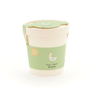 Beiger Becher mit grünem Etikett, auf dem eine gezeichnete Gans und der Text „Gans lieben Dank“ zu sehen ist.