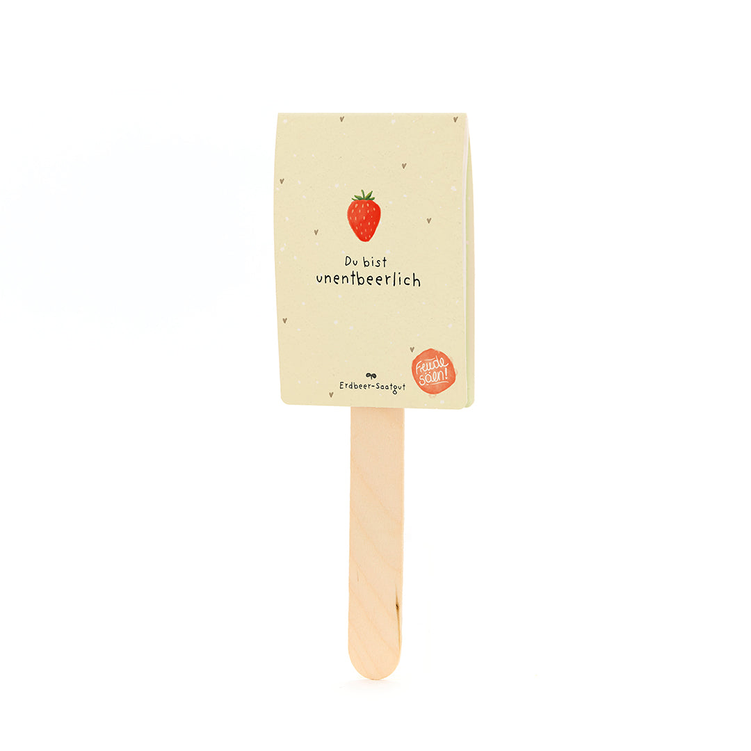Holzstab mit einem Etikett, das eine Erdbeere und den Text „Du bist unentbeerlich“ sowie „Erdbeer-Saatgut“ zeigt.