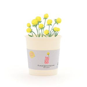 Becher mit gelben GummibĂ€rchen-Blumen und einem Etikett, auf dem âGummibĂ€renblume fĂŒr dichâ steht.