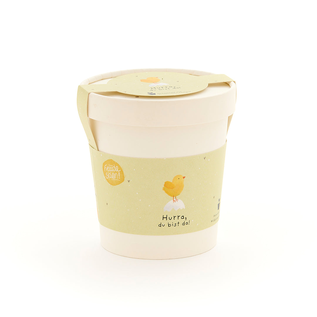 Becher mit gelbem Etikett, darauf ein Küken und die Aufschrift "Hurra, du bist da!"