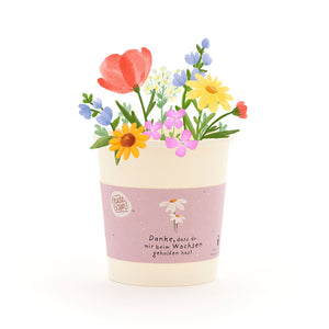 Ein Blumentopf mit bunten, gezeichneten Blumen und einer Banderole, auf der steht: "Danke, dass du mir beim Wachsen geholfen hast."