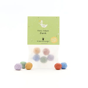 Tüte mit bunten Samenbällchen und grünem Etikett, darauf eine gezeichnete Gans und der Text "Gans lieben Dank – Wildblumensaatgut".