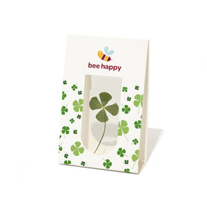 Papiertüte mit vierblättrigem Kleeblatt und dem Text "bee happy" sowie einer Bienenillustration.