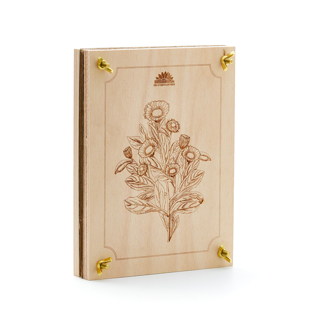 Holzbuch mit floralem Gravurmuster und goldenen Metallecken, stehend auf weißem Hintergrund.