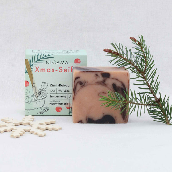 Handgemachte Seife mit Zimt-Kakao-Duft neben ihrer Verpackung und Weihnachtsdekoration.