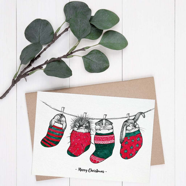 Weihnachtskarte mit gezeichneten Tieren in festlichen Socken, Eukalyptuszweig und "Merry Christmas"-Schriftzug.