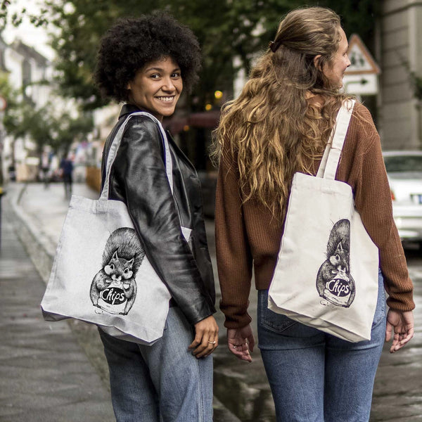 Zwei lächelnde Frauen, die sich umdrehen und Stofftaschen mit einem Katzenbild tragen.