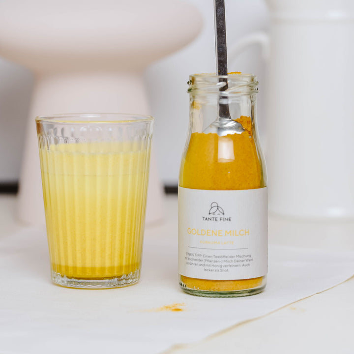 Ein Glas mit goldener Milch neben einer Flasche Kurkuma-Latte auf einer Küchenoberfläche.