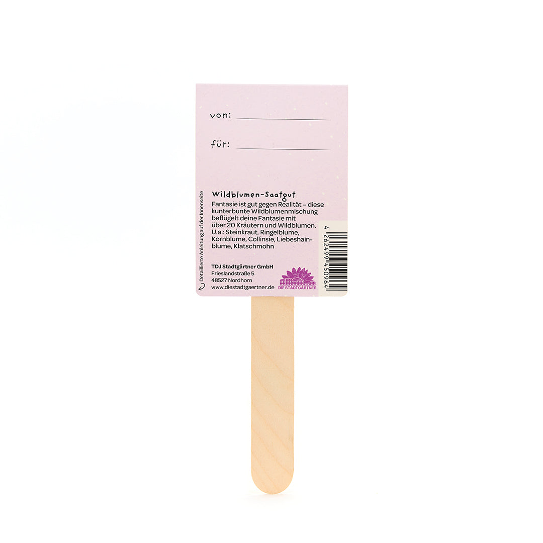 Holzstäbchen mit einem rosa Etikett, auf dem "von" und "für" steht sowie Informationen über Wildblumen-Saatgut auf Deutsch.