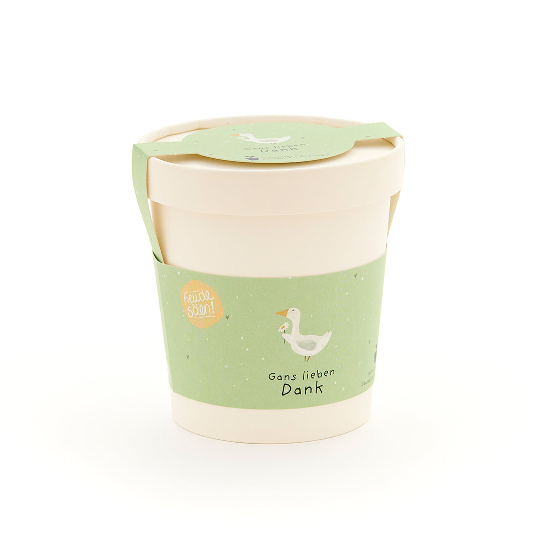 Beiger Becher mit grünem Etikett, auf dem eine gezeichnete Gans und der Text „Gans lieben Dank“ zu sehen ist.