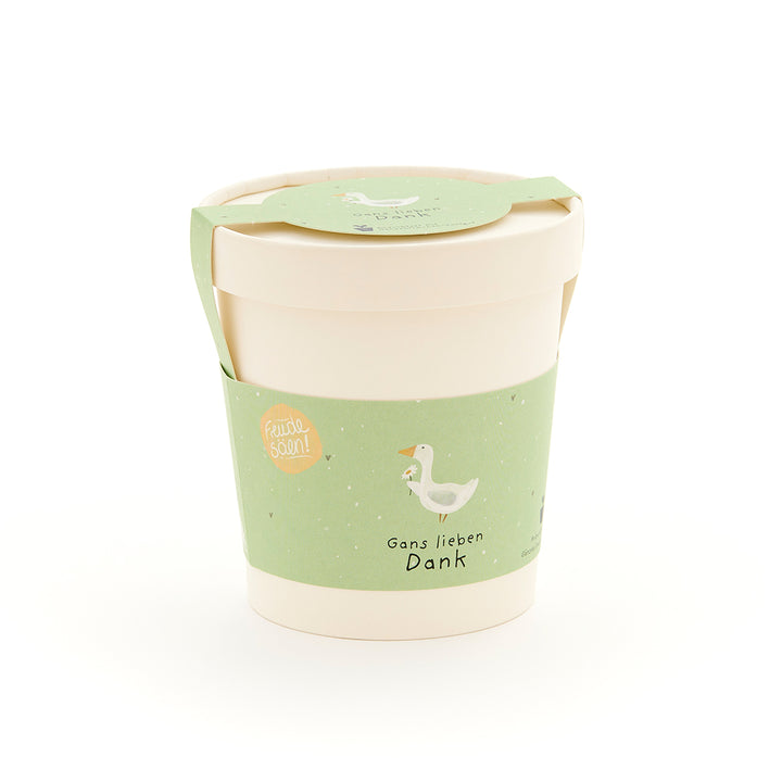 Beiger Becher mit grünem Etikett, auf dem eine gezeichnete Gans und der Text „Gans lieben Dank“ zu sehen ist.