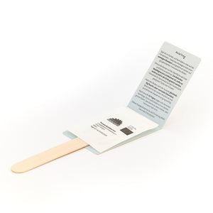 Ein Holzstab mit einer aufgeklappten Verpackung, in der sich eine Tüte mit Samen und eine gedruckte Anleitung in deutscher Sprache befinden.