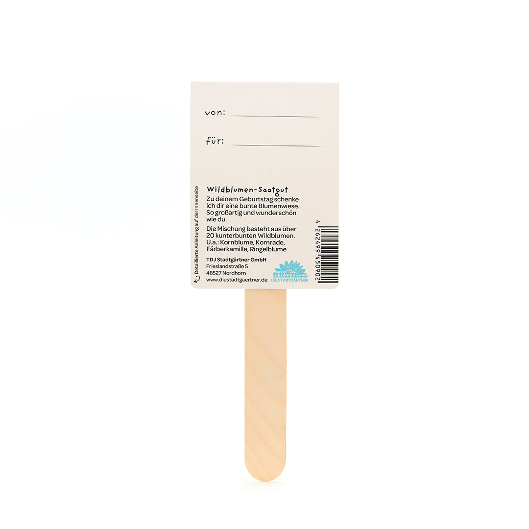 Rückseite eines Wildblumen-Saatgut-Geschenks mit Holzstab, Feldern für "von" und "für", sowie Beschreibung der Blumensamenmischung auf Deutsch.