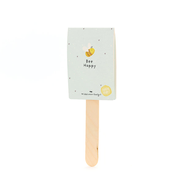 Holzstab mit hellblauem Etikett, darauf eine gezeichnete Biene und der Text "Bee Happy"; Wildblumen-Saatgut.