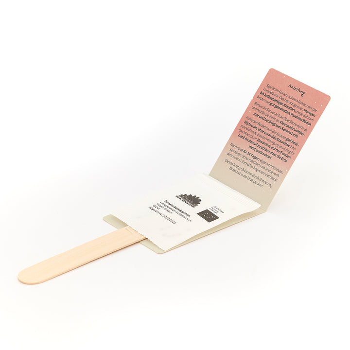Ein Holzstab mit einer beigelegten Samenpackung und einer aufgeklappten Anleitung in deutscher Sprache.