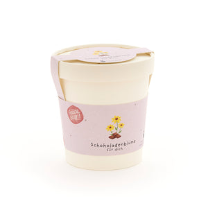 Pflanzbecher mit rosa Etikett, auf dem "Schokoladenblume für dich" und eine Zeichnung einer Blume über einem Schokoladenstück zu sehen ist.