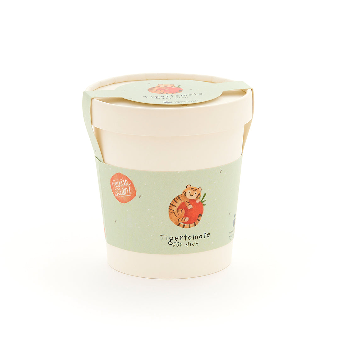 Becher mit grünem Etikett, auf dem ein Tiger mit einer Tomate und der Text "Tigertomate für dich" abgebildet ist.