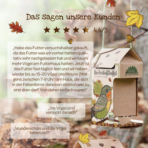 Kundenzitate und Bewertungen zum Bio-Vogelfutter neben einem dekorativen Vogelhaus aus Karton mit herbstlichen Blättern im Hintergrund.