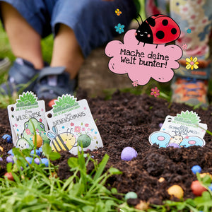 Zwei Kinder pflanzen bunte Samenbomben im Garten; Schilder mit Illustrationen von Bienen und Schmetterlingen stecken in der Erde. Ein gezeichneter Marienkäfer mit Sprechblase sagt: "Mache deine Welt bunter!"
