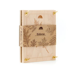 Holzpresse für Blätter mit botanischen Gravuren und braunem Papierband, darauf Blattmotive und der Schriftzug „Blattpresse“.