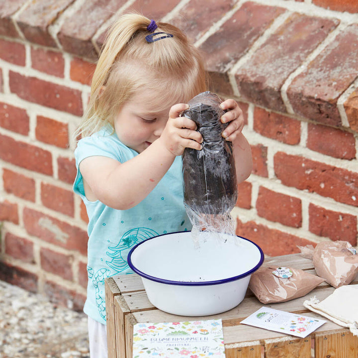 Kleines Mädchen gießt Wassser von einer Flasche in eine Schüssel beim Gärtnern.