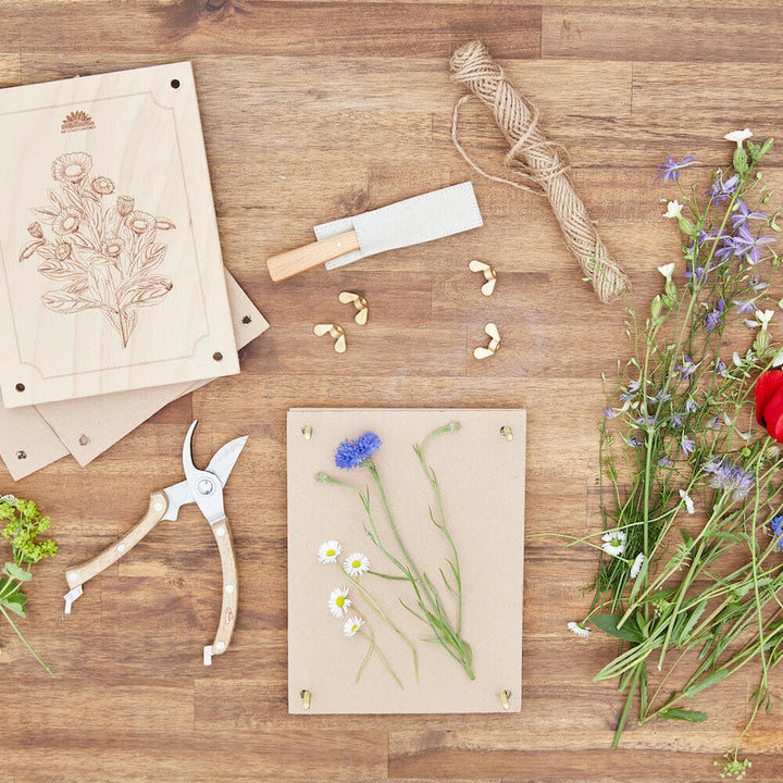 Bastelmaterialien und gepresste Blumen auf einem Holztisch.
