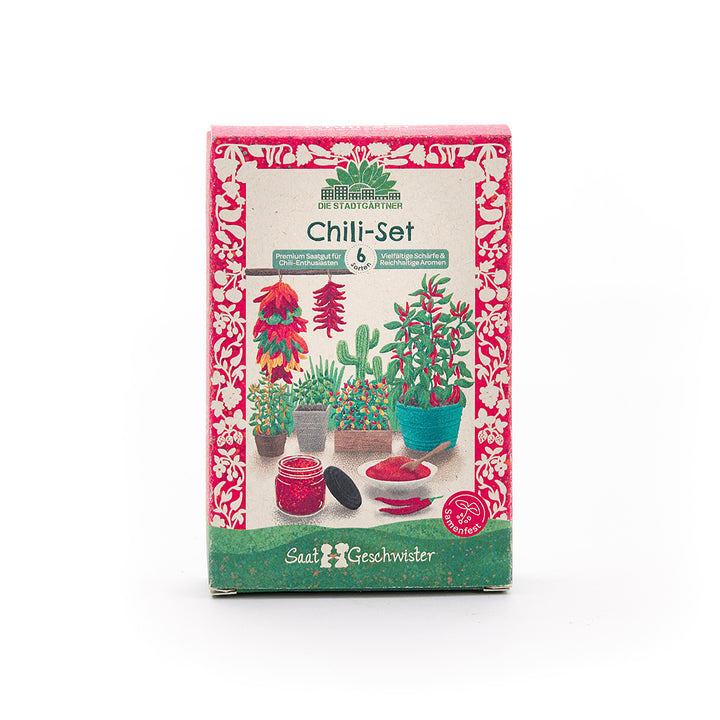 Verpackung eines Chili-Sets mit bunten Illustrationen von Chili-Pflanzen, Töpfen, Chili-Schoten und einem Glas Chilipulver, umlaufend mit rotem Blumenmuster.