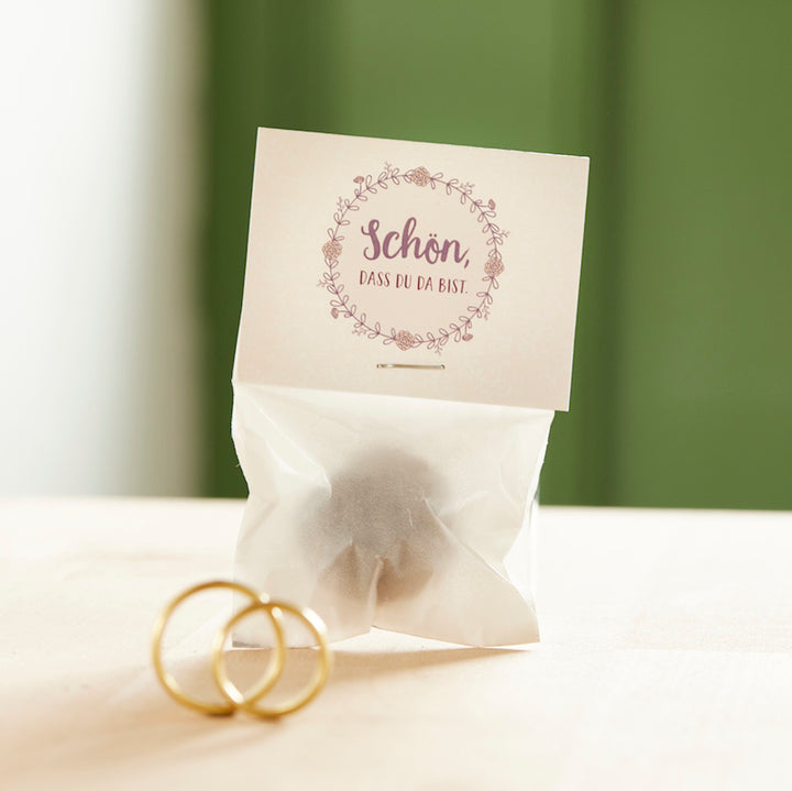 Kleine Tüte mit der Aufschrift "Schön, dass du da bist" und zwei goldenen Eheringen davor.