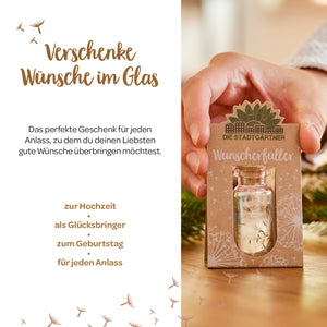 Person hält eine kleine Geschenkkarte mit der Aufschrift "Wunscherfüller" und einem kleinen Glasfläschchen, umgeben von saisonaler Dekoration und Text, der Geschenkideen für verschiedene Anlässe präsentiert.