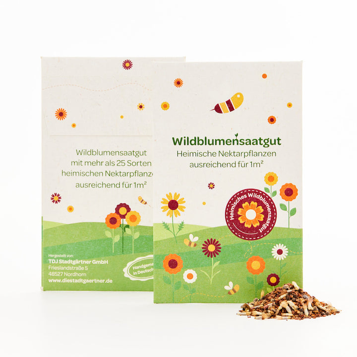 Zwei Packungen Wildblumensaatgut mit buntem Blumen- und Bienenmotiv sowie ein kleiner Haufen Saatgut davor.