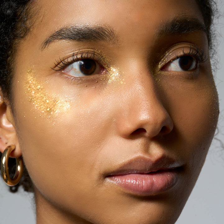 Nahaufnahme eines Gesichts einer Person mit gold-glitzerndem Make-up um die Augen.