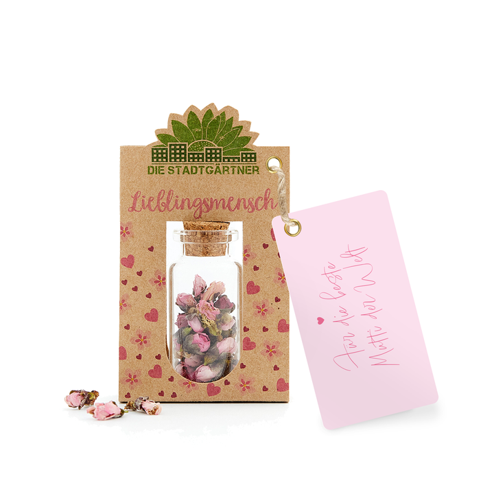 Geschenkanhänger mit der Aufschrift "Lieblingsmensch" und ein kleines Glasfläschchen mit getrockneten Blumen auf einem Kraftpapier-Hintergrund neben einer rosa Karte mit Herz und "Für Dich".