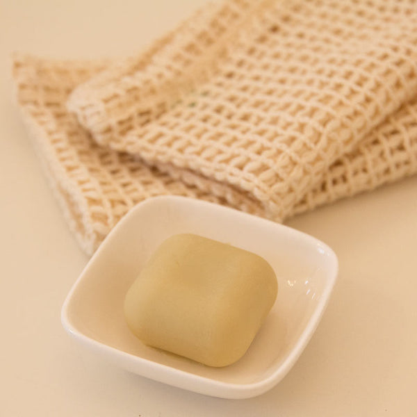 Stück Seife in einer kleinen Schale mit einem gefalteten Tuch im Hintergrund.