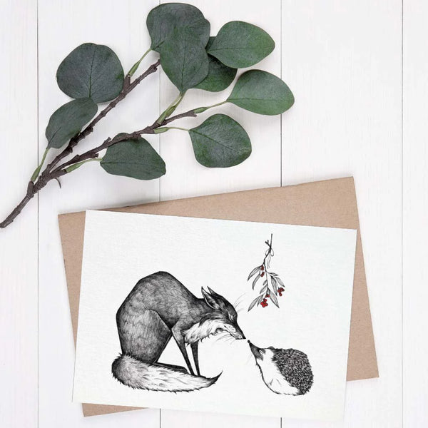 Zeichnung eines Fuchses, der einen Igel küsst, auf einer Grußkarte neben einem Eukalyptuszweig und einem Umschlag.