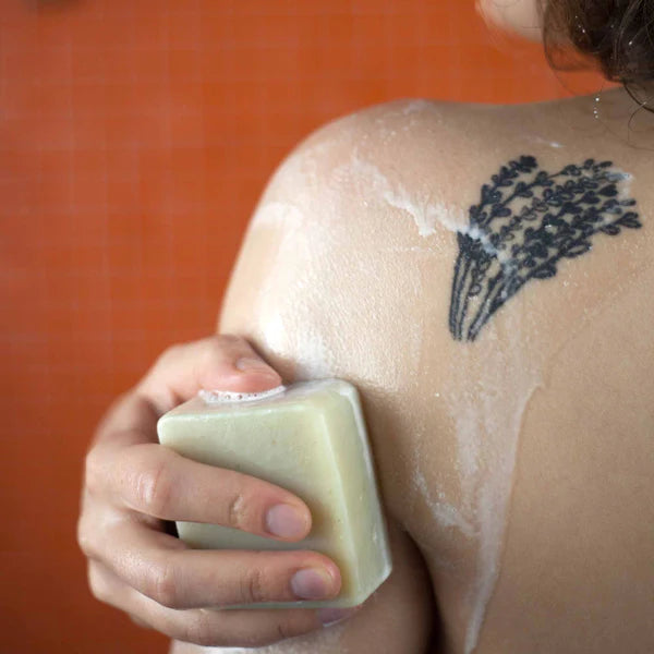 Person verwendet Seife auf der Haut mit einem sichtbaren Tattoo auf der Schulter.
