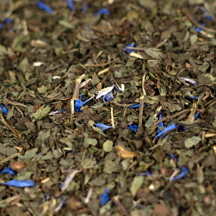 Nahaufnahme von losen Teeblättern mit blauen Blütenblättern.