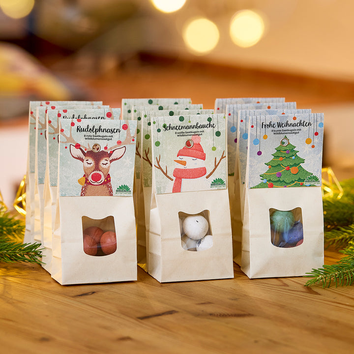 Drei weihnachtlich dekorierte Tüten mit Süßigkeiten auf einem Holztisch, jeweils mit den Aufschriften „Rudolphnasen“, „Schneemannbäuche“ und „Frohe Weihnachten“.