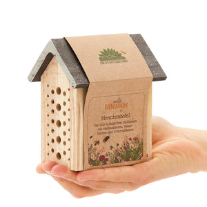 Eine Hand hält ein kleines Bienenhotel aus Holz, mit der Aufschrift "Aktion Bienenwohl Bienenhotel" auf Deutsch.