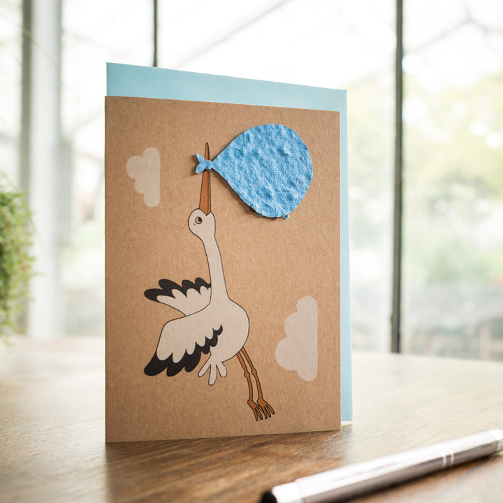 Handgefertigte Grußkarte mit Storch, der ein blaues Bündel trägt, auf einem Tisch mit Stift.