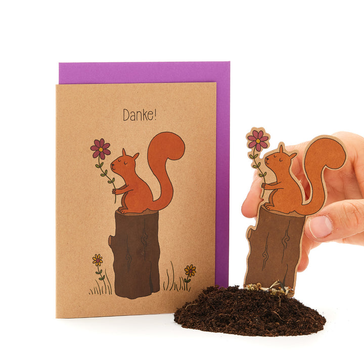 Eine Hand hält eine Ausschneidefigur eines Eichhörnchens neben einer Dankeskarte mit einem ähnlichen Eichhörnchenmotiv.