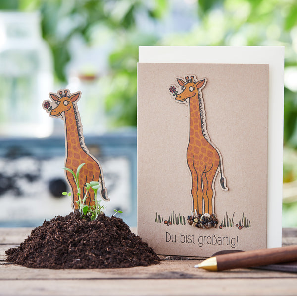 Glückwunschkarte mit Giraffenmotiv und der Aufschrift "Du bist großartig!", neben einem Haufen Erde und einem Bleistift.