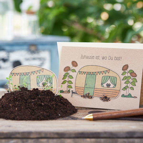 Handgezeichnete Glückwunschkarte mit Campingwagen und Blumen neben einer Schaufel und Erde.