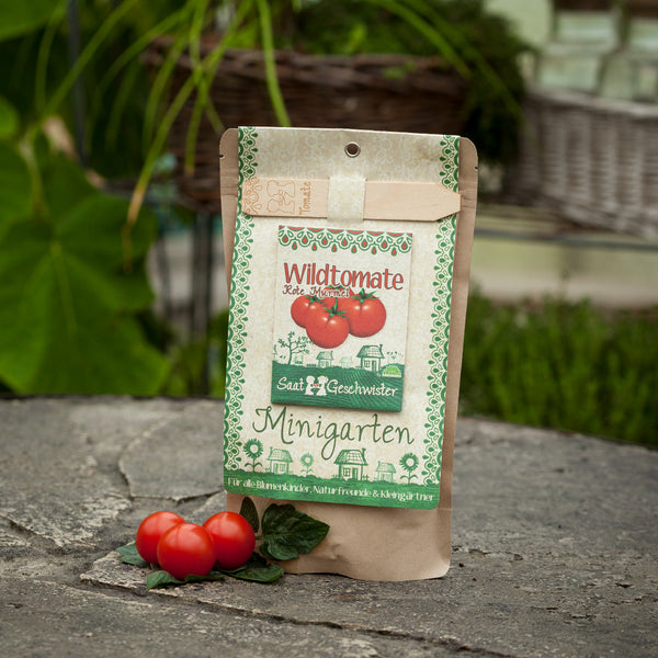 Verpackung für Wildtomatensamen "Rote Murmel" auf einem Steinboden mit frischen Tomaten daneben.