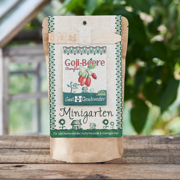Verpackung für Goji-Beeren Saatgut mit der Aufschrift 'Minigarten' vor einem Gewächshaus.