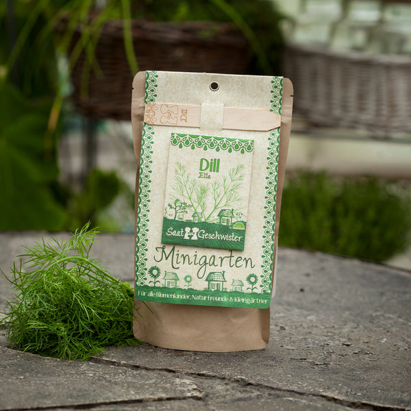 Verpackung für Dillsamen mit der Bezeichnung "Minigarten" neben frischem Dill auf einer Steinplatte.