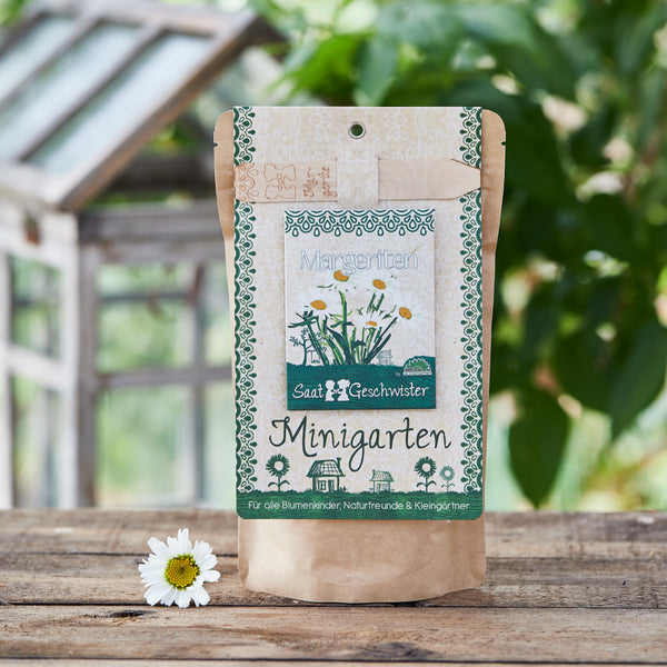 Papiertüte mit Aufschrift "Minigarten" für Gartenliebhaber vor Gewächshauskulisse.