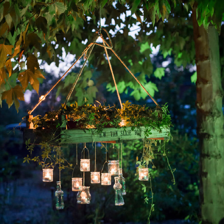Hängender Holzrahmen mit Pflanzen und Kerzen in Gläsern beleuchtet im Abendlicht