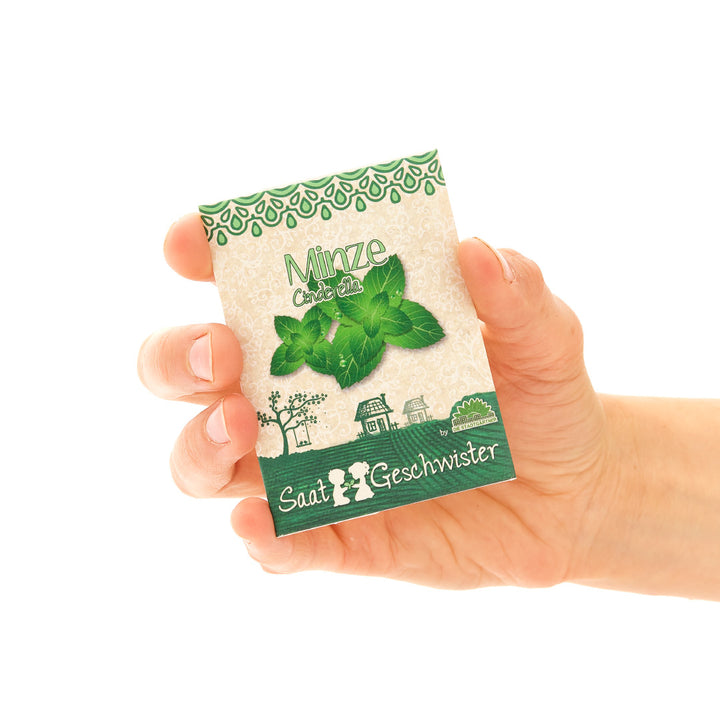 Eine Hand hält eine Packung Minzsamen mit der Aufschrift "Minze", umgeben von grüner Gestaltung und dem Untertitel "Saat-Geschwister".